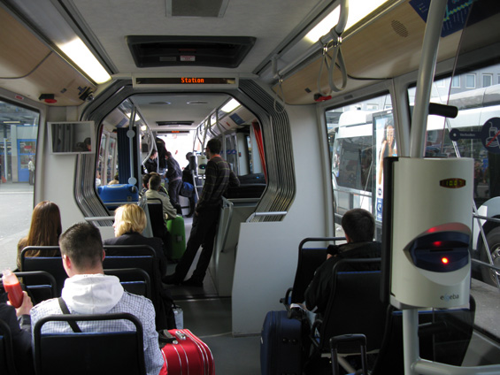Druhý pohled do interéru metrobusu Phileas. V autobusu jsou také odkladové plochy na zavazadla - vzhledem k charakteru linky 401 velmi praktické. Ve voze se nachází jak oznaèovaè na klasické papírové zónové jízdenky "Strippenkaart" tak terminál na národní èipové karty. LCD obrazovky ukazují nejen aktuální trasu vozidla, ale i pøedpokládaný dojezd na koneènou a také nejbližší odjezdy vlakù z hlavního nádraží.