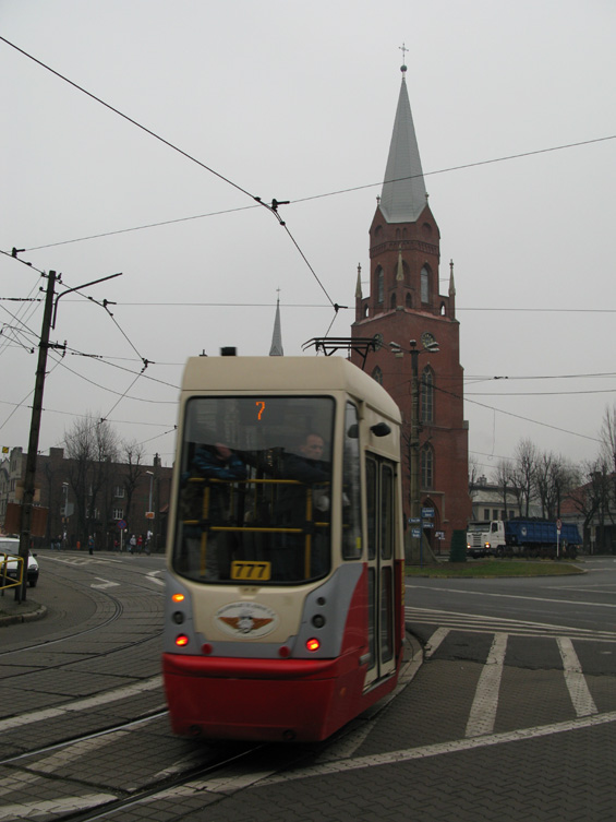 Modernizovaná tramvaj na lince 7 pøed kostelem v Szopienicích, které leží na cestì mezi Katowicemi a Sosnowcem. Linka 7 tu konèí, dál pokraèují linky 14 do Myslowic a nejdùležitìjší linka 15 pøes Sosnowiec do Zagórze. Na èást spojù jsou vypravovány dvojice, jinak na vìtšinì linek v této oblasti jezdí sólovozy. Nedaleko tohoto místa se odpojuje linka 14, která pak podjíždí železnièní tra� velmi fotogenickým tunýlkem.