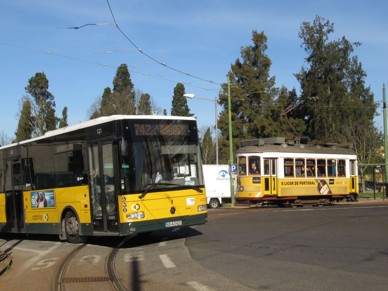 Setkání staršího autobusu Mercedes-Benz s tramvají Remodelados na koneèné linek 25 a 28 u høbitova ve ètvrti Prazeres západnì od centra. Tramvaje i autobusy provozuje v Lisabonu dopravce Carris, což dokládá totožné barevné øešení vozidel.