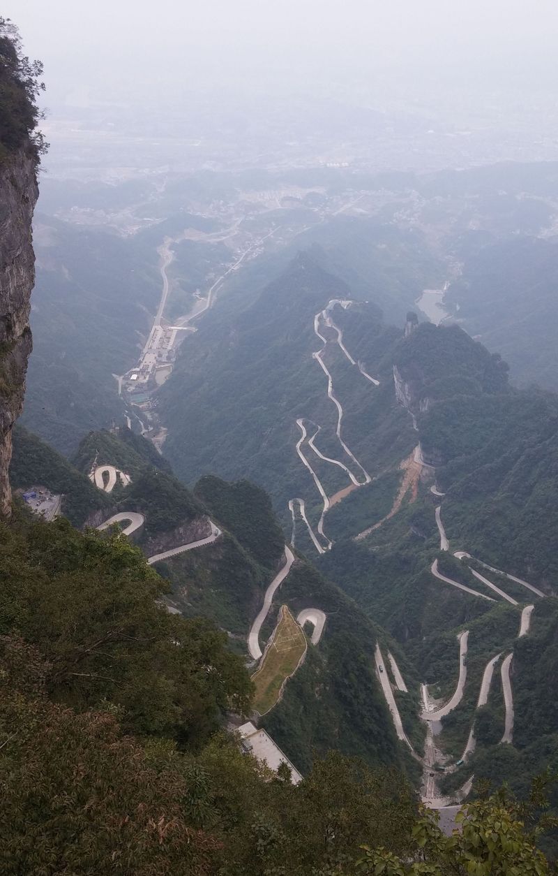 A takto vypadá již zmíněná silnice z horního konce obřího schodiště s 999 schody. Kdesi dole v dálce je město Zhangjiajie, kam vás dopraví buďto další zelené mikrobusy a nebo lanovka.